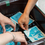 將明信片輕放入水箱中，清洗掉藥水後，隨著雙氧水的洗禮，藍晒圖像逐漸浮現。